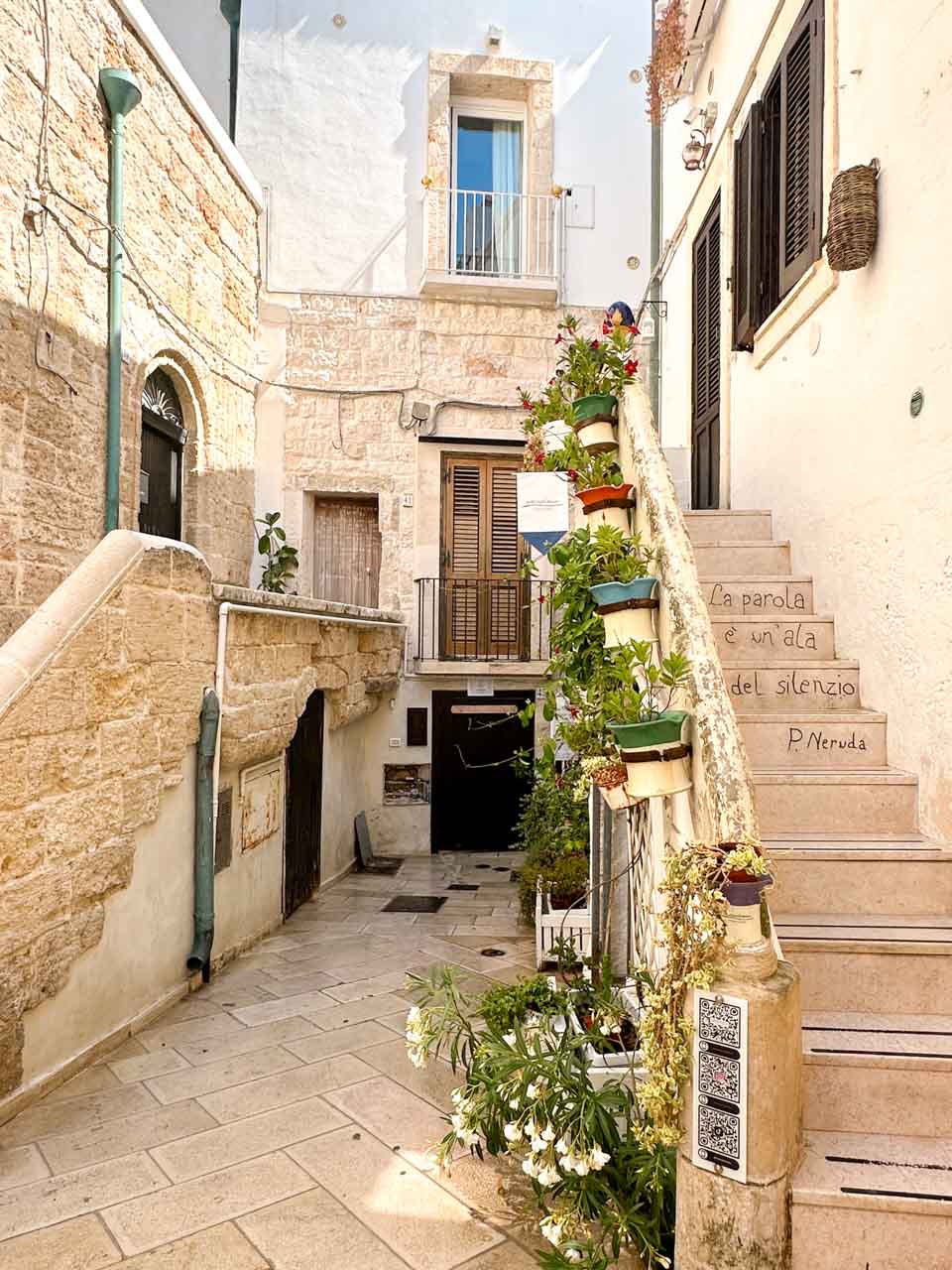 Quiet alley in Polignano a Mare with stone walls, balconies, and potted plants