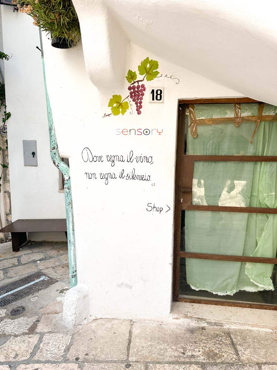 White wall with an Italian quote, grape illustration, and a bar entrance in Polignano a Mare