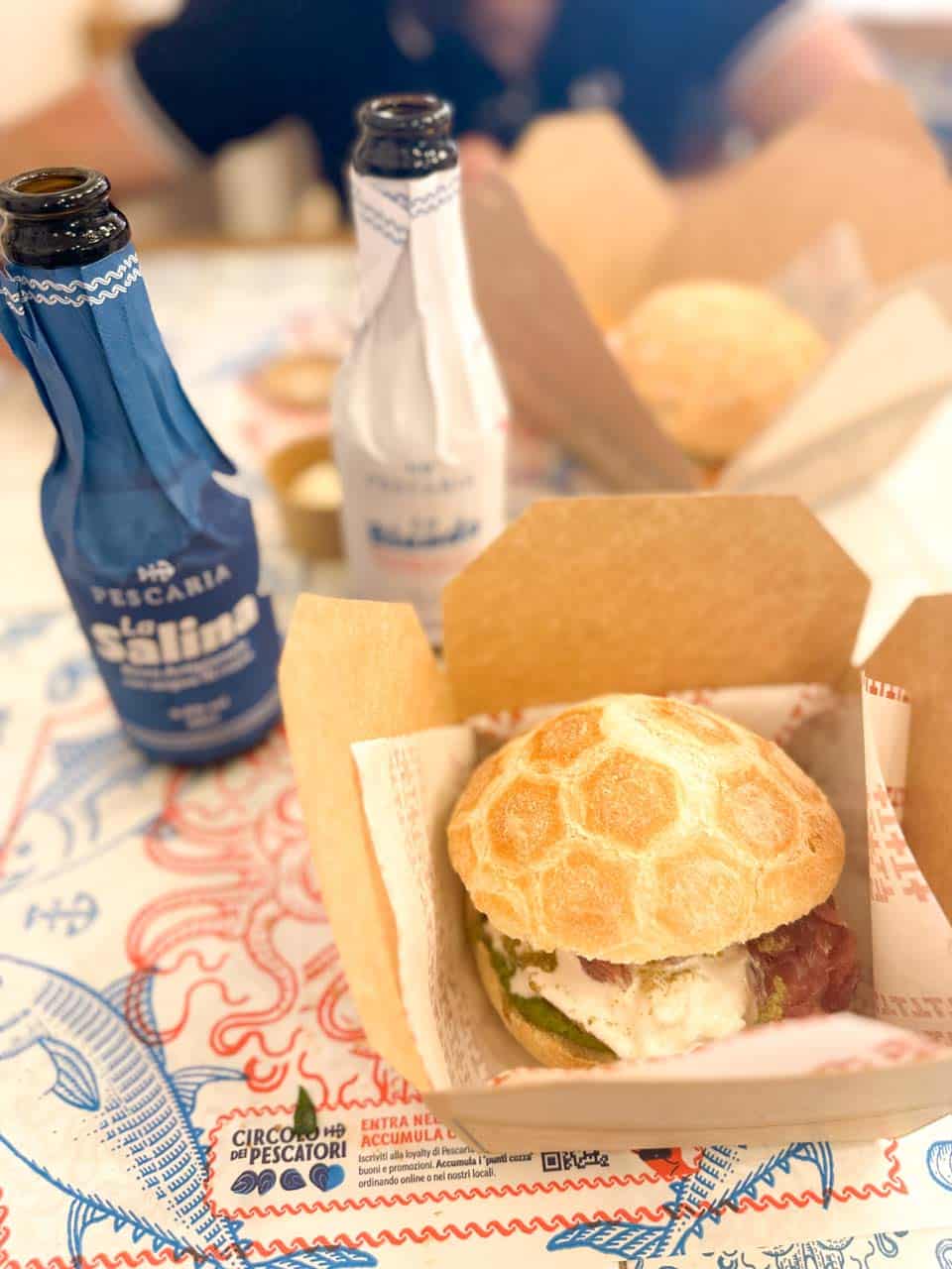 A sandwich with tuna tartare, stracciatella cheese, and basil pesto, served in a box with drinks at Pescaria in Polignano a Mare