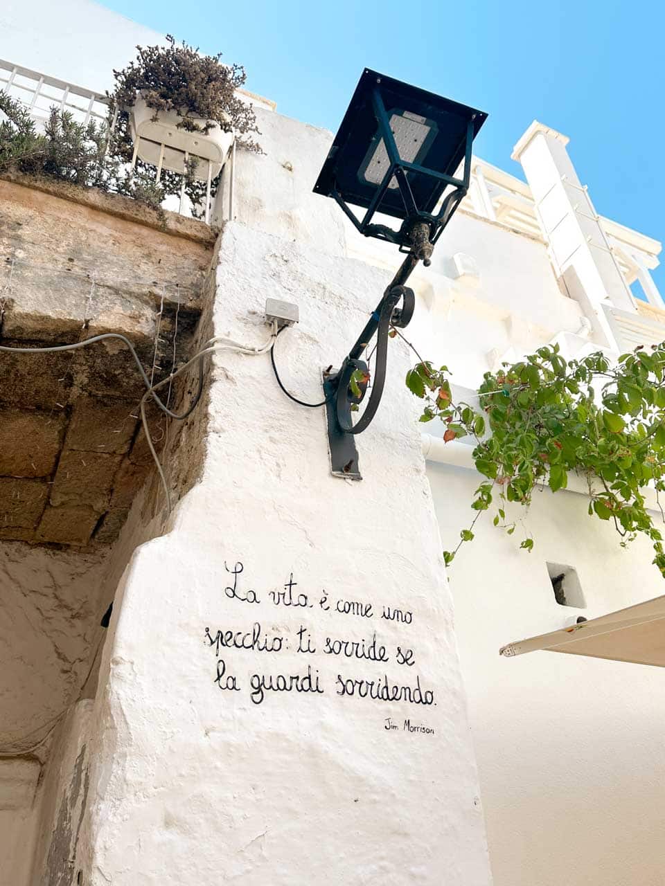 White wall with an Italian quote by Jim Morrison and a traditional street lamp in Polignano a Mare