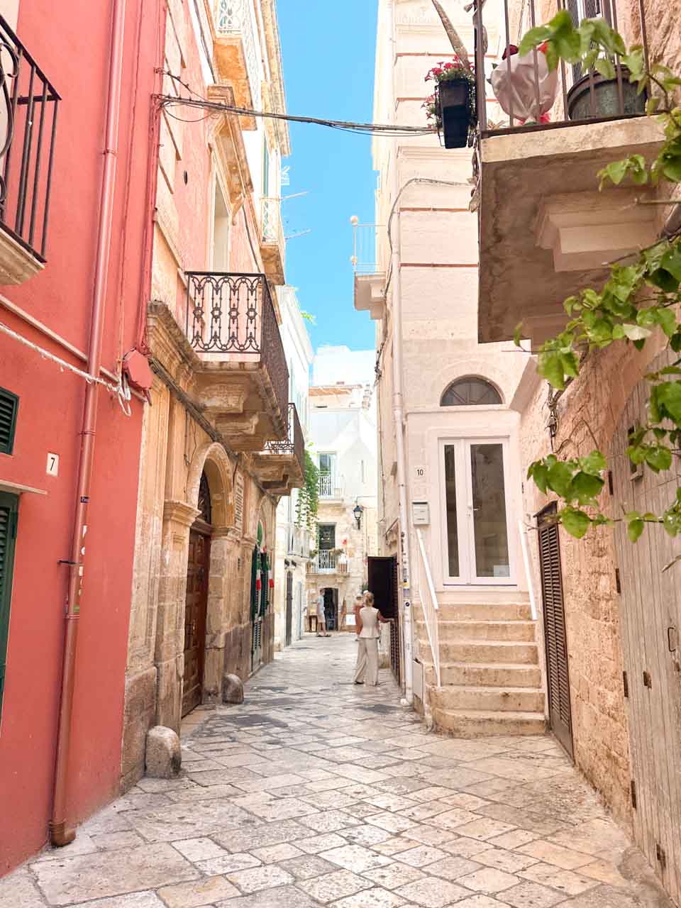 Narrow street in Polignano a Mare with stone buildings, balconies, and a person walking