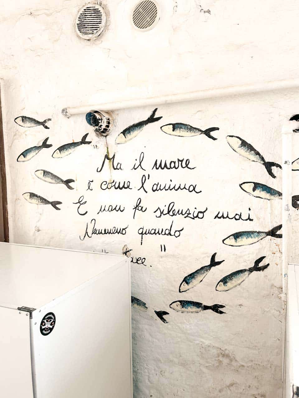 White wall with painted fish and an Italian quote in Polignano a Mare