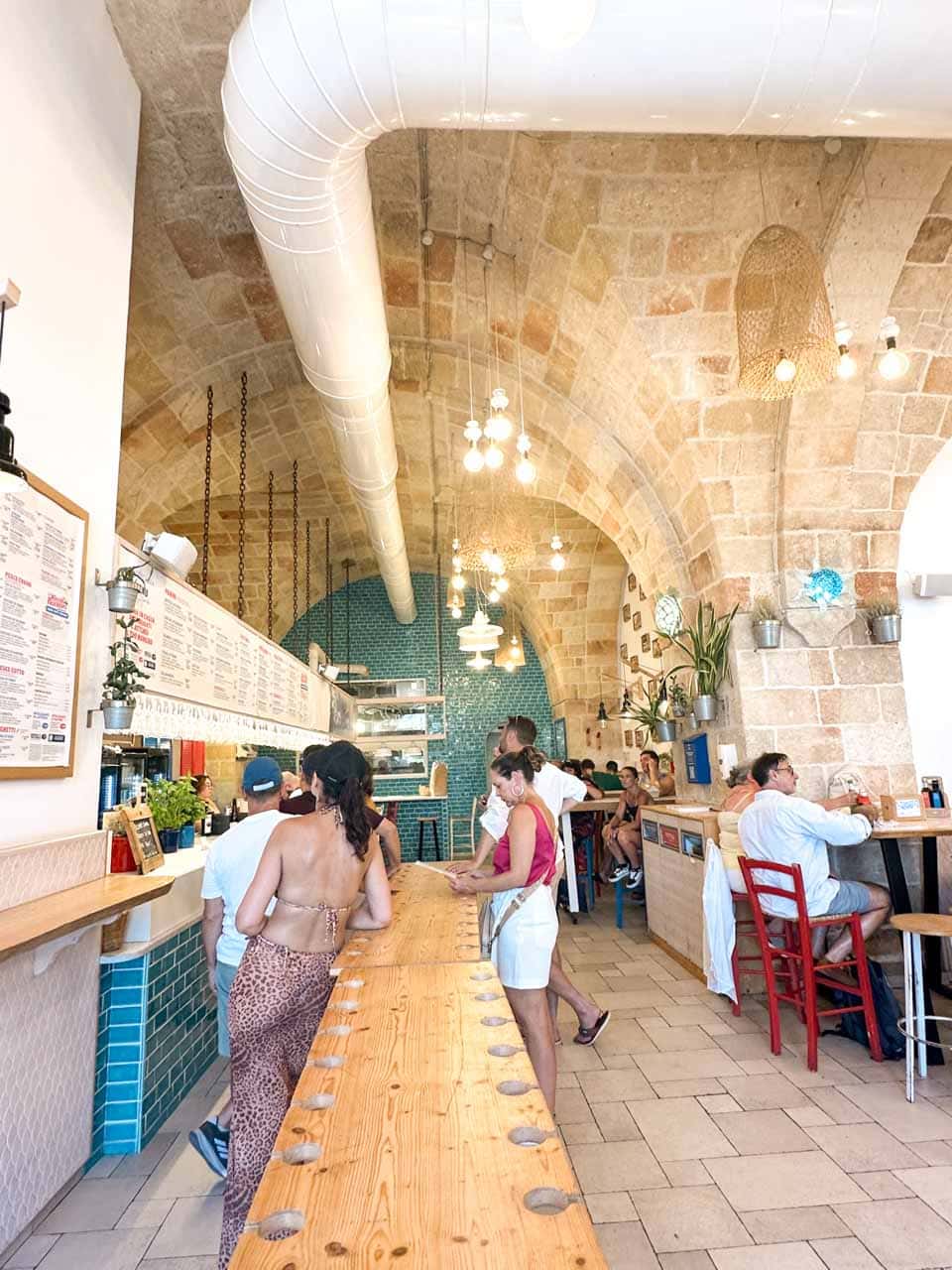 Busy interior of Pescaria with wooden tables, stone arches, and people dining in Polignano a Mare