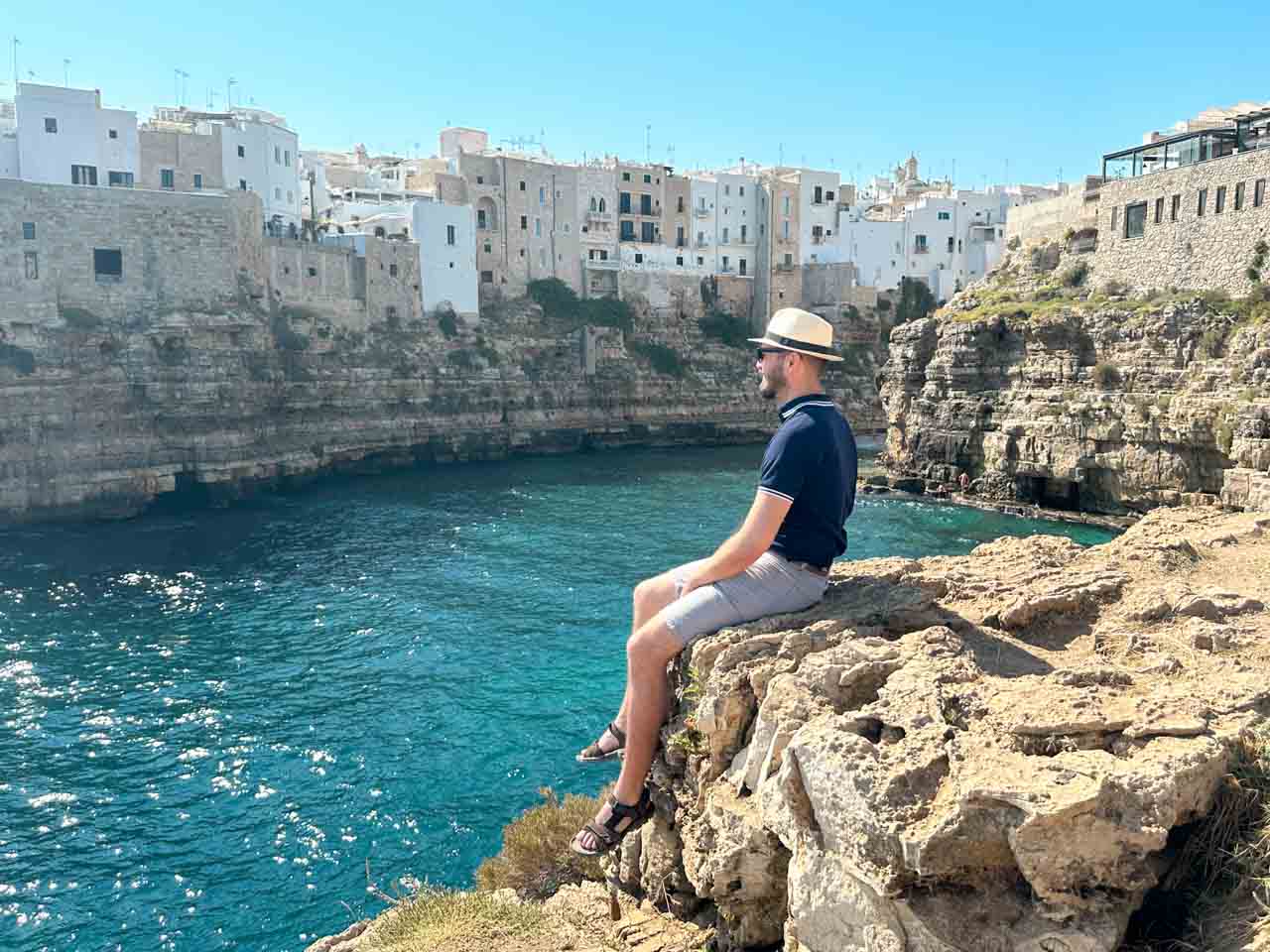 Man sitting on a rocky cliff overlooking the turquoise sea and old town in Polignano a Mare