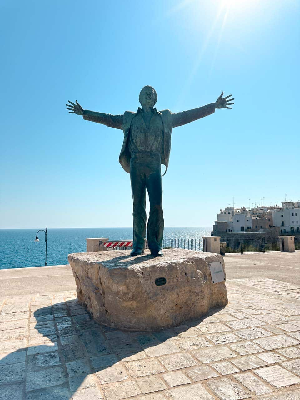 Statue of Domenico Modugno with arms raised overlooking the sea in Polignano a Mare, Italy