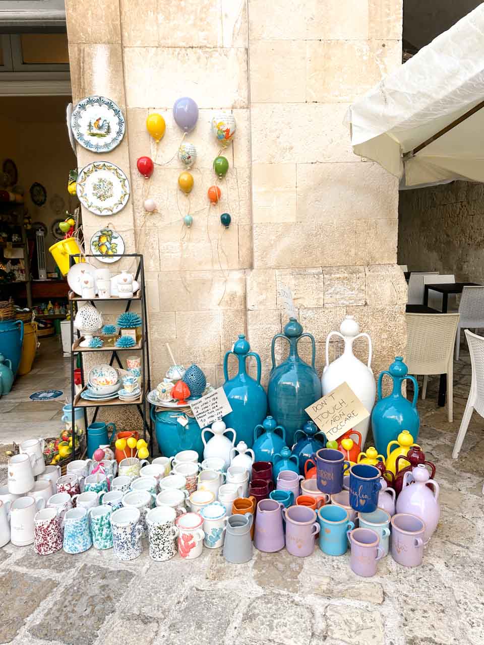 Colourful ceramic jugs, cups, and plates displayed outside a shop in Polignano a Mare