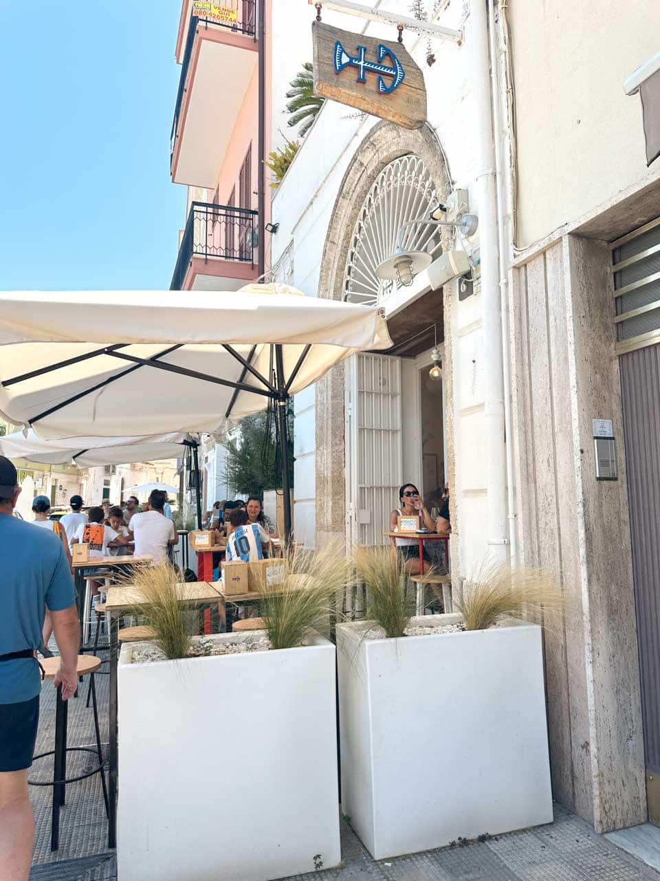 Outdoor seating at Pescaria with tables under umbrellas on a sunny street in Polignano a Mare, Italy
