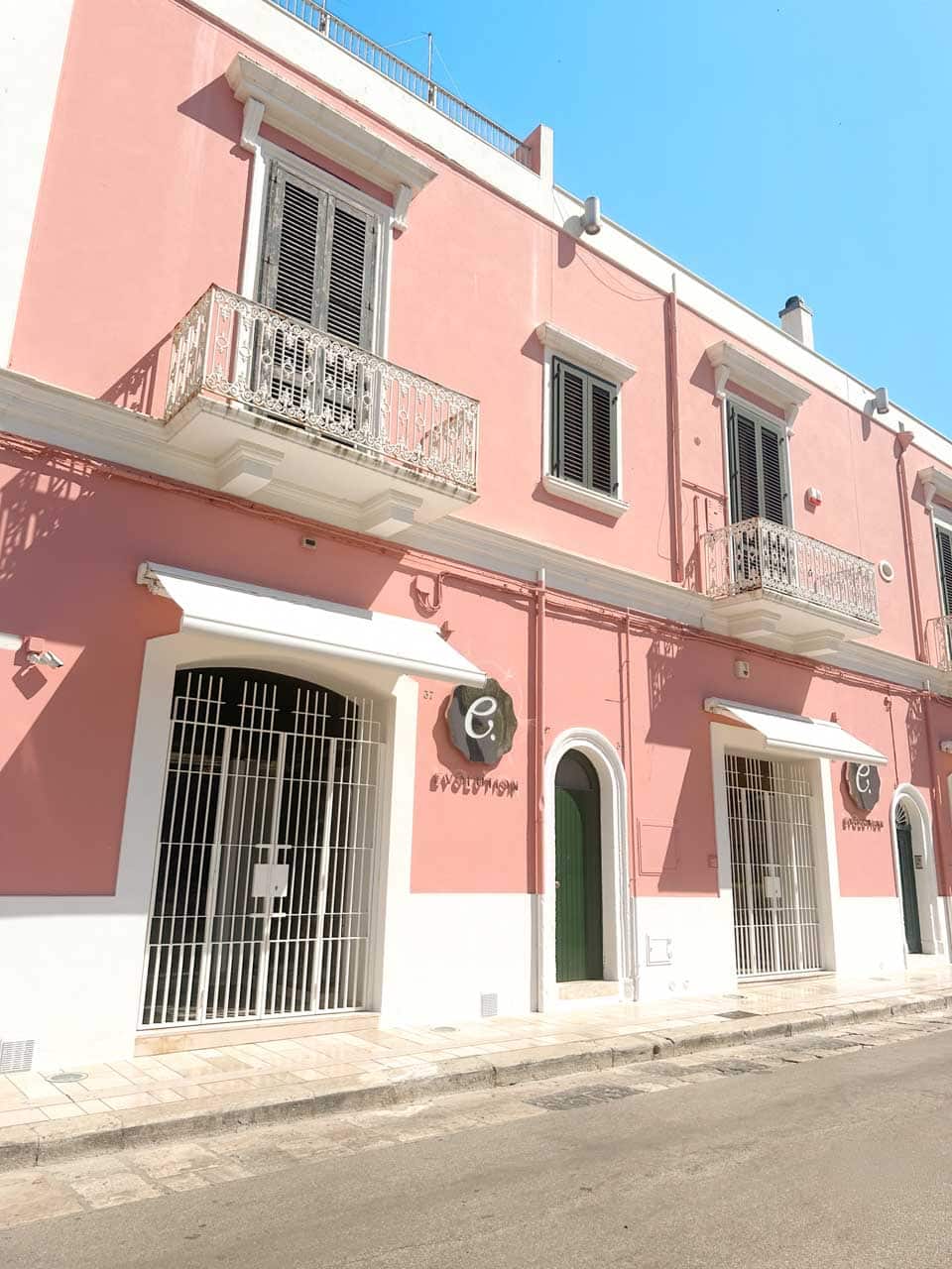 Pastel pink building with white balconies and green shutters in Polignano a Mare