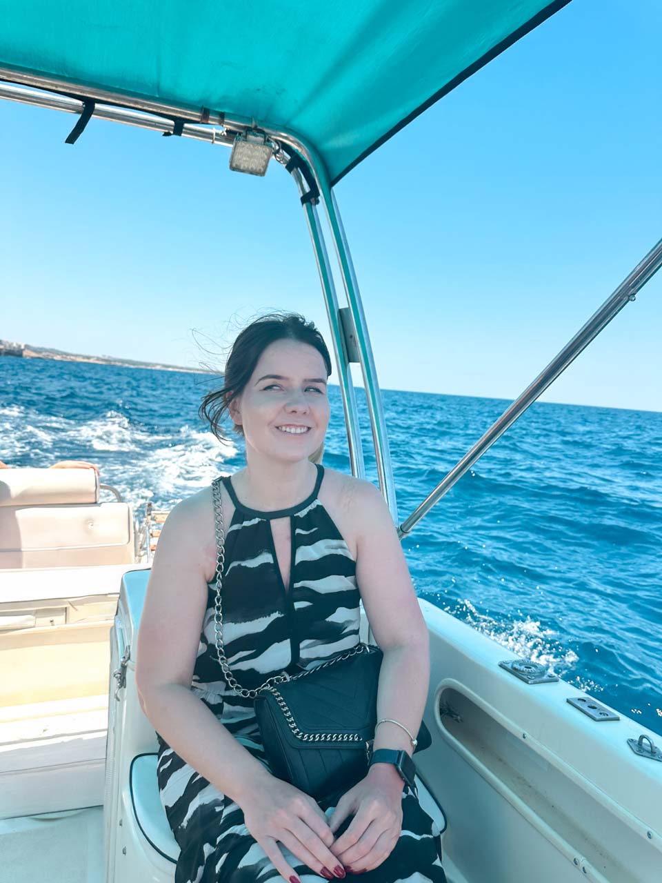 Woman in a black and white maxi dress sitting on a boat with views of the Adriatic Sea near Polignano a Mare