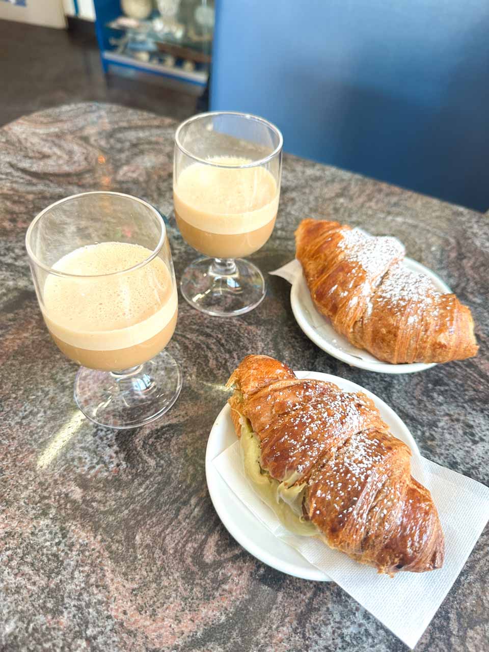 Two glasses of caffe speciale and two cream-filled croissants on a table at The Super Mago del Gelo Mario Campanella in Polignano a Mare