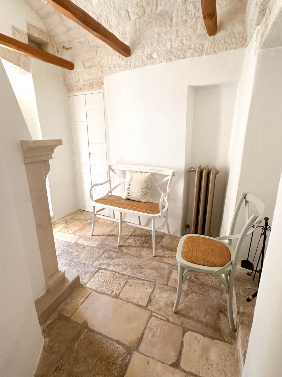Stone-floored sitting area inside a restored trullo with white walls and woven-seat chairs