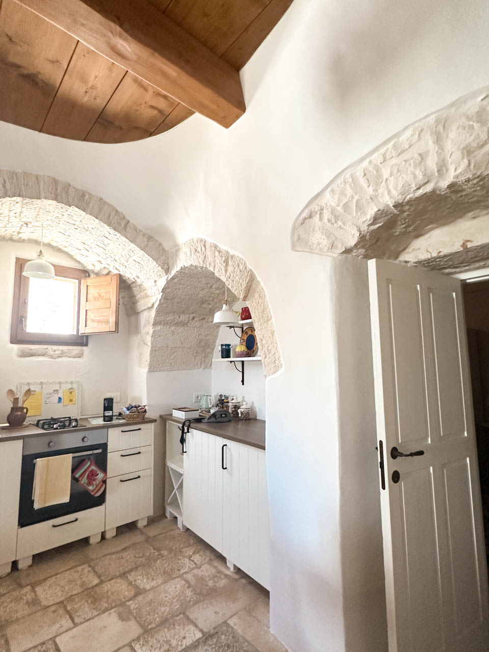 Kitchen inside a restored trullo with stone arches, wooden beams, and traditional features