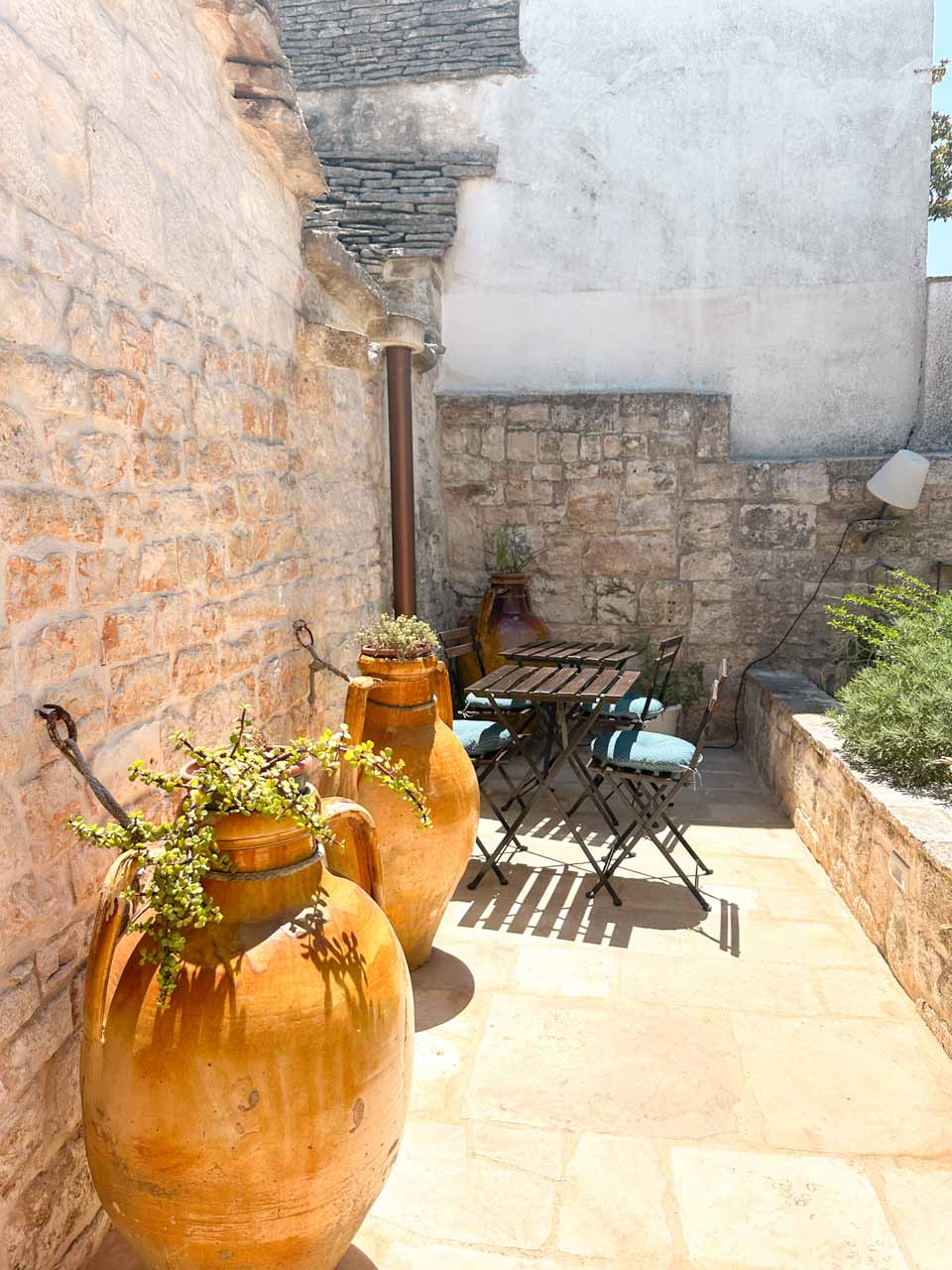 Small courtyard beside a trullo with terracotta pots, stone walls, and outdoor seating
