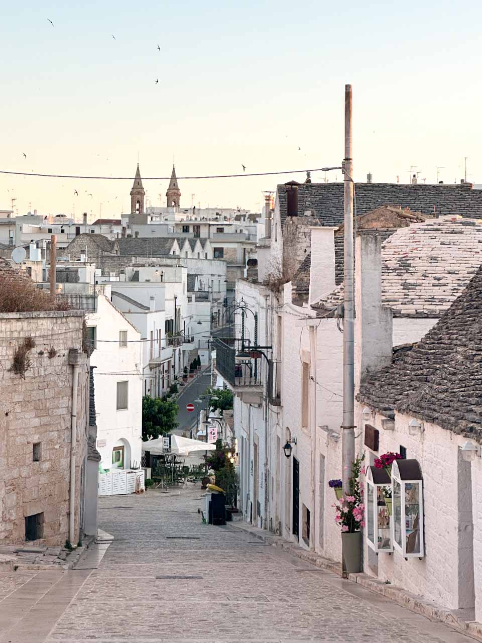 View down a quiet Alberobello street with trulli roofs and the Basilica of Saints Cosmas and Damian in the distance