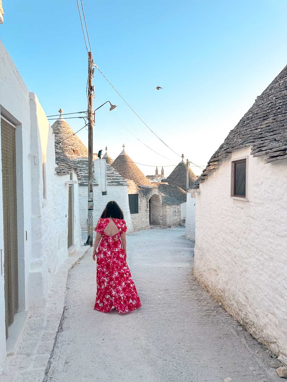 Woman in a pink, red, and white dress walking between traditional trulli houses in Alberobello