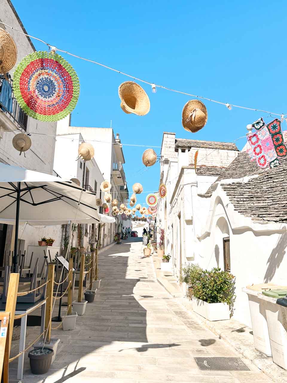 Street decorated with hanging straw hats and colourful crochet ornaments in Alberobello
