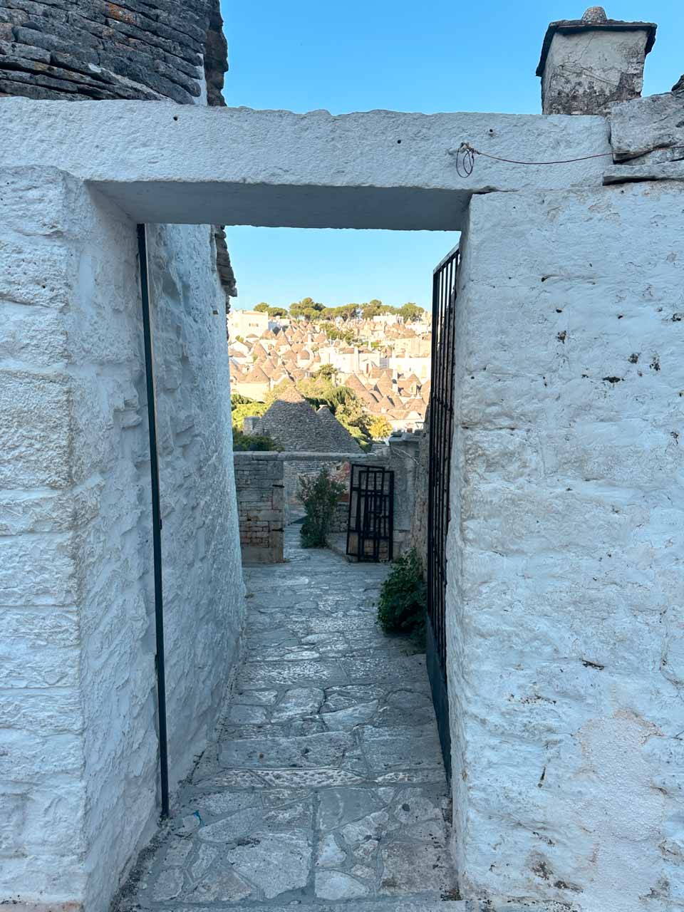 Stone pathway framed by white walls leading to a view of trulli rooftops