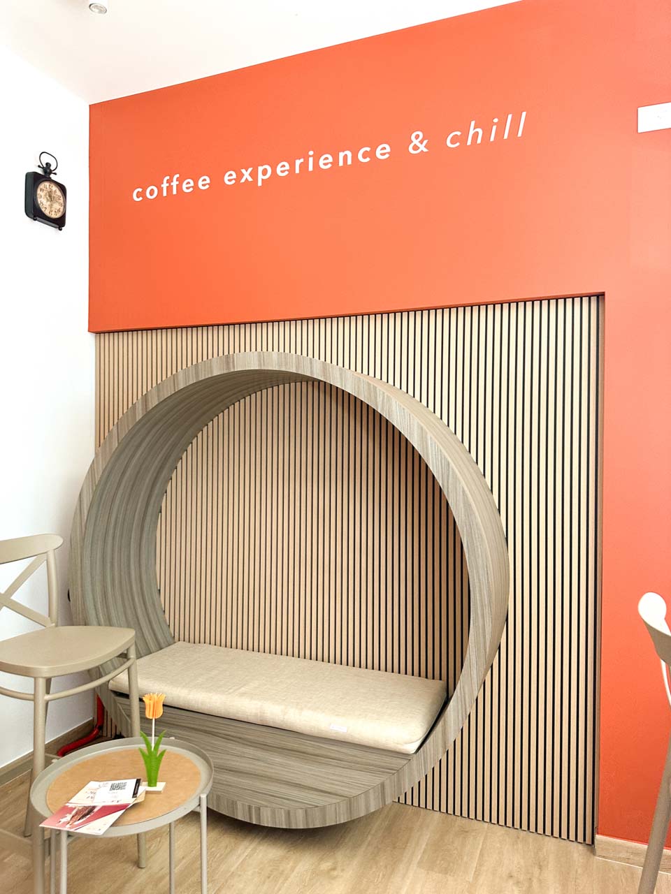 Curved wooden seating area inside Cols – Coffee Experience & more in Alberobello with a 'coffee experience & chill' sign on the wall