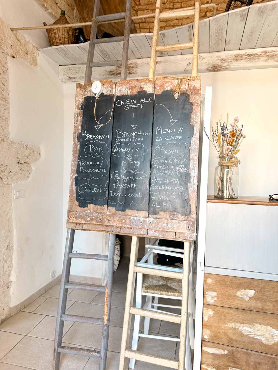Rustic interior of Così Com’era in Alberobello with wooden ladders and a chalkboard menu