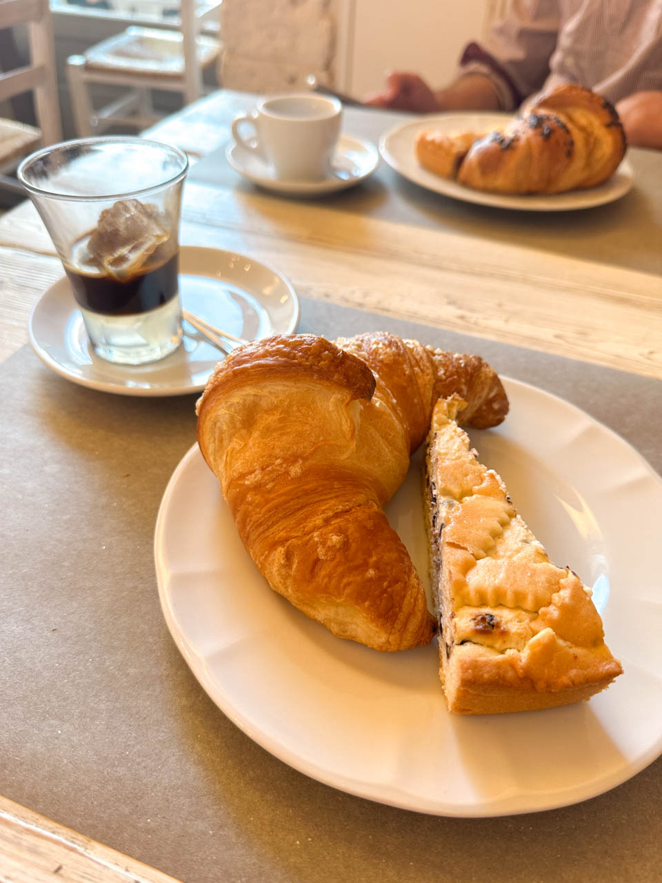 A croissant and a slice of cake with iced coffee on a table at Così Com’era in Alberobello, Italy