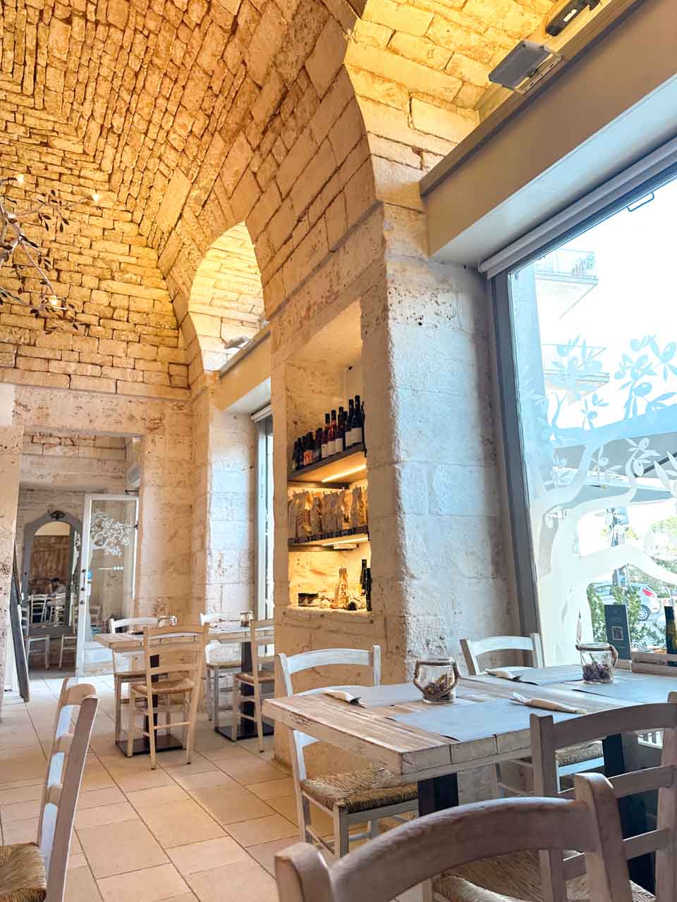 Rustic interior of Così Com’era in Alberobello, Italy with stone arches and wooden tables