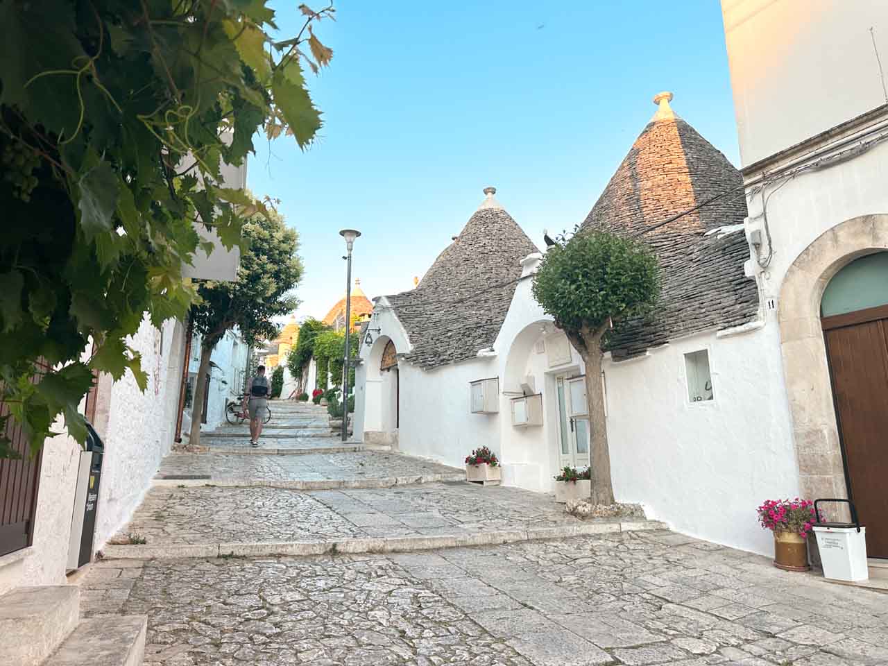 Trulli-lined street with stone steps and a person walking in Alberobello, Italy