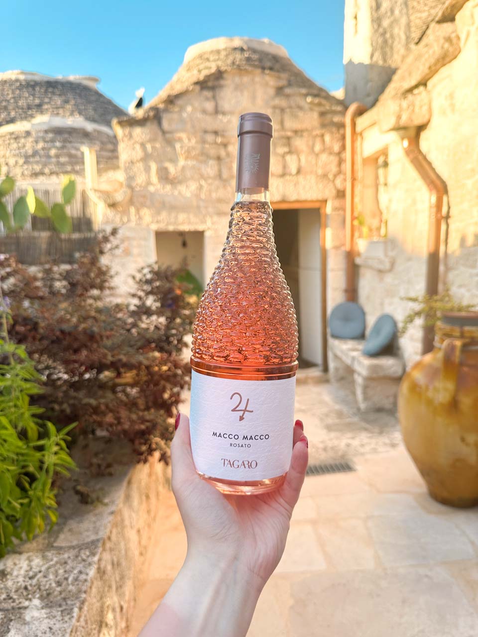 Bottle of rosé wine held in front of a trullo courtyard at sunset