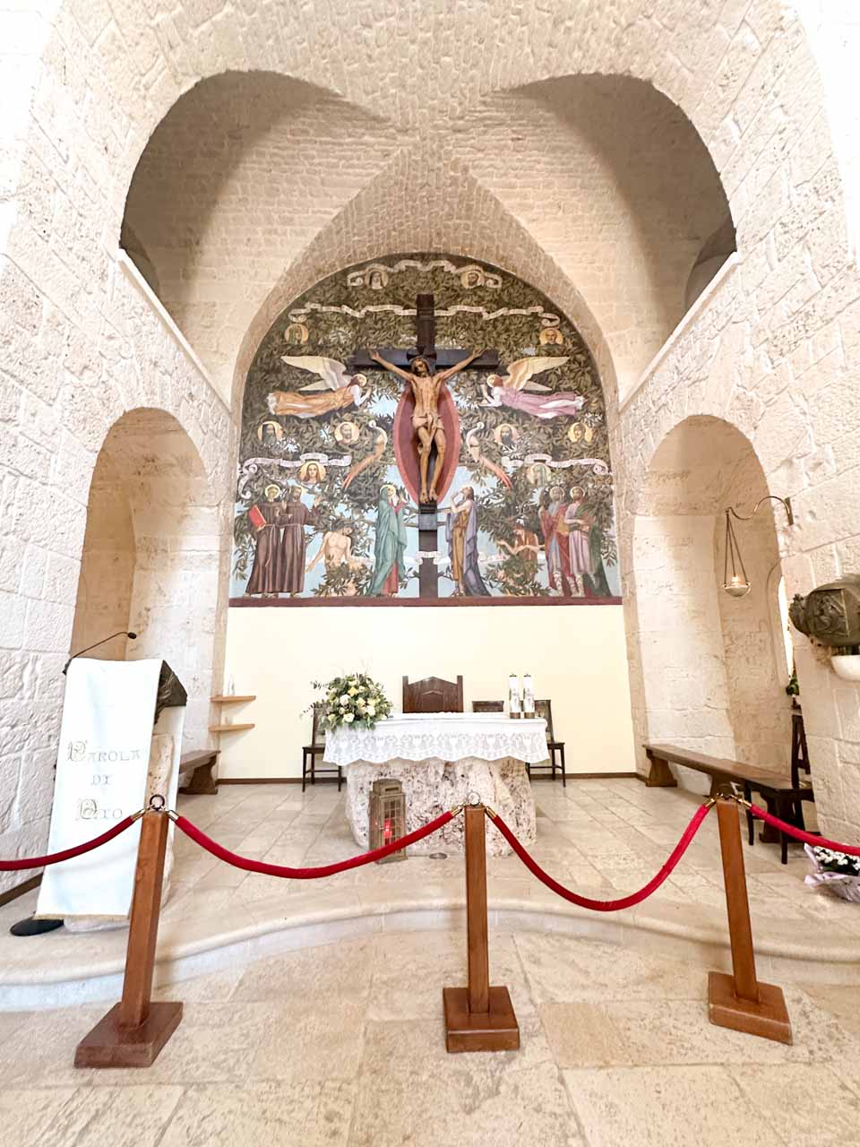 Interior of the Church of Saint Anthony (Chiesa di Sant’Antonio) in Alberobello with stone arches, an altar, and a crucifix mural