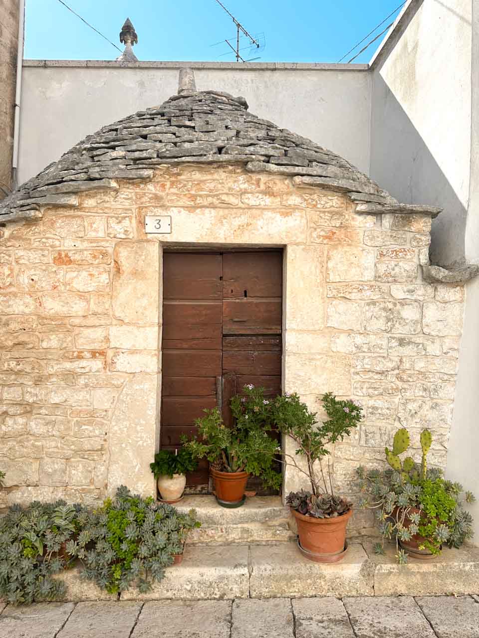 Traditional stone trullo with potted plants outside the wooden front door