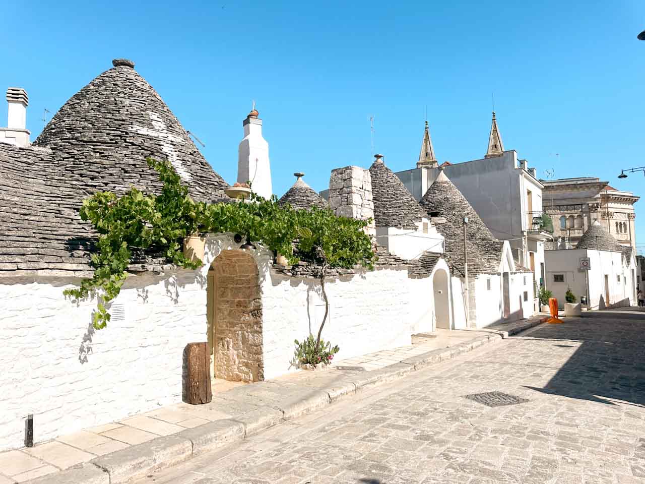 Historic trulli houses along a sunlit street in the Rione Aia Piccola district of Alberobello