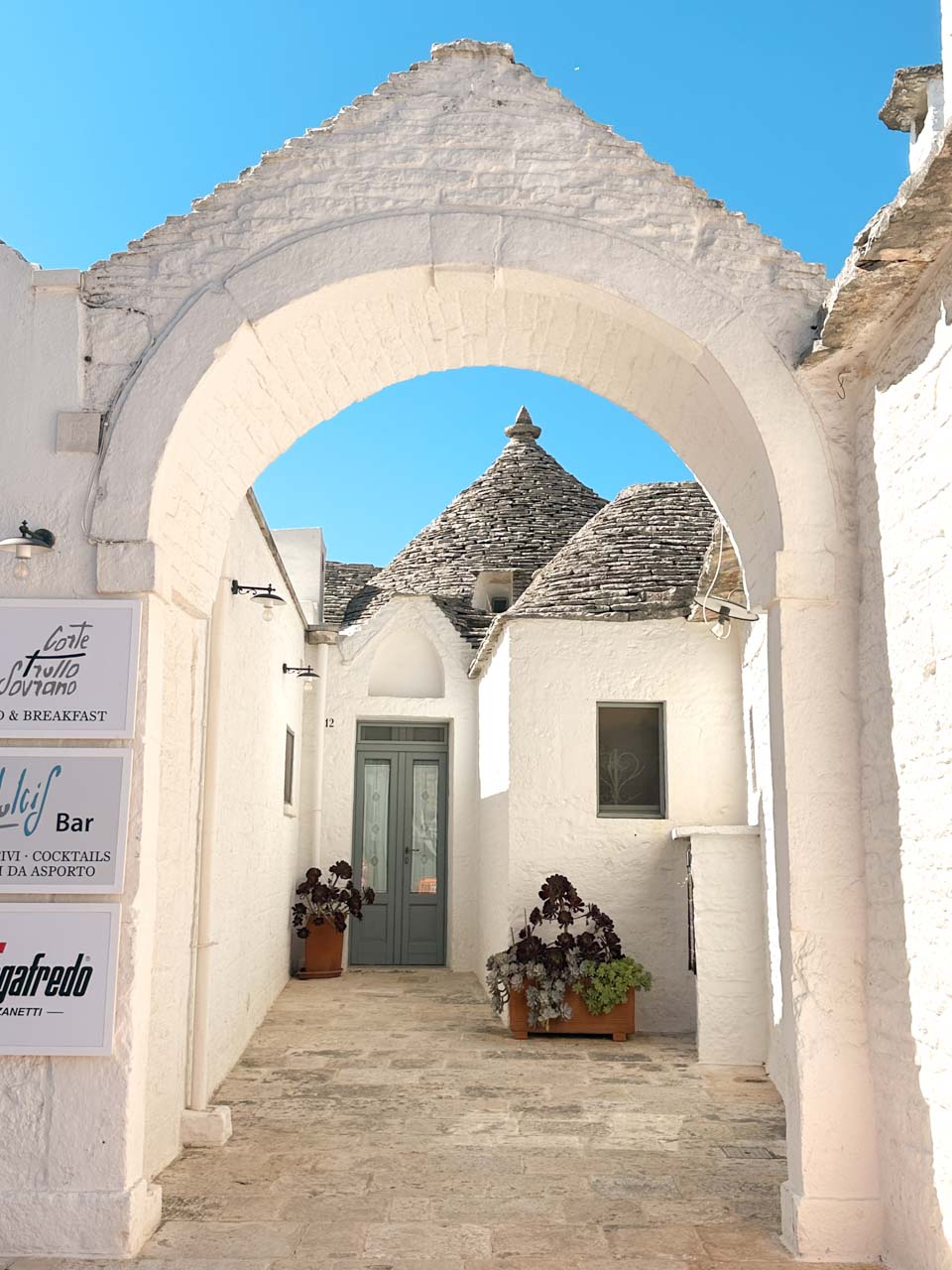 White stone archway framing a traditional trullo house in Alberobello