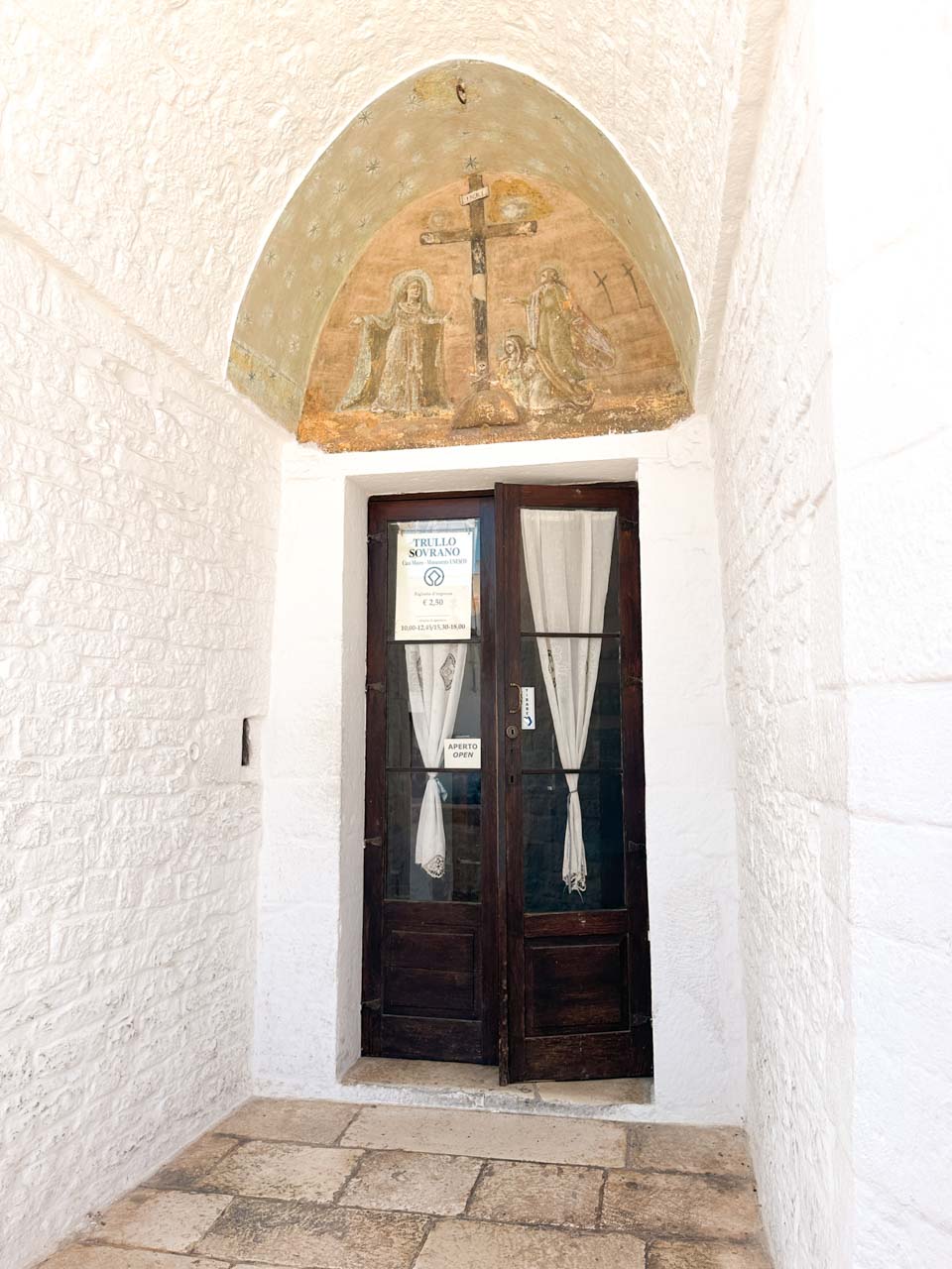 Entrance to Trullo Sovrano beneath a historic fresco and stone archway