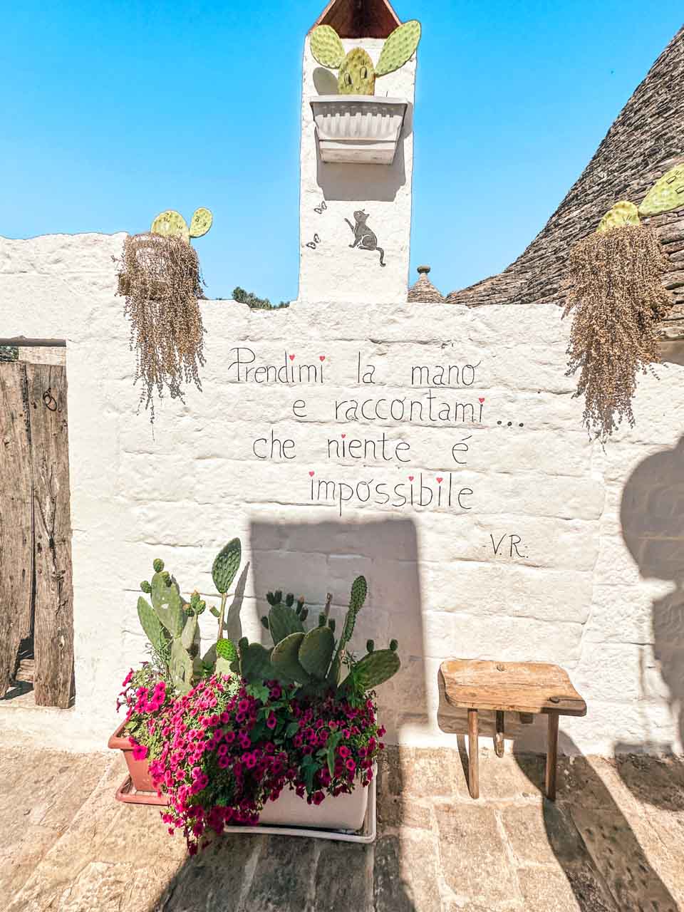 Whitewashed wall with an Italian quote, cacti, and bright pink flowers in Alberobello