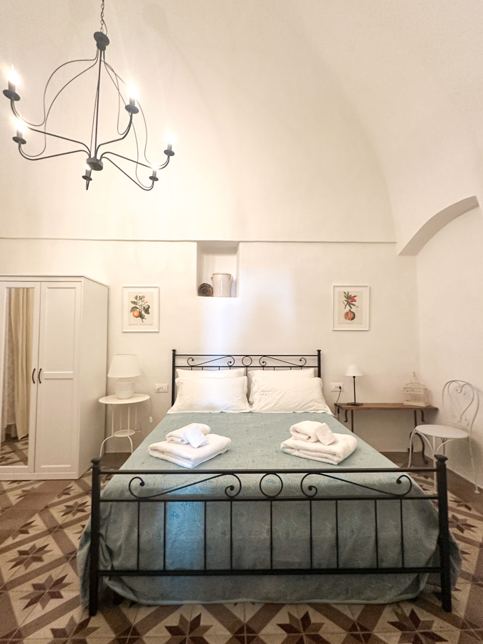 Bedroom inside a restored trullo with a vaulted ceiling, patterned floor tiles, and a wrought-iron bed