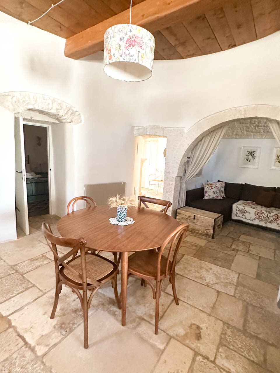 Dining area inside a restored trullo with stone arches, a wooden table, and a seating nook