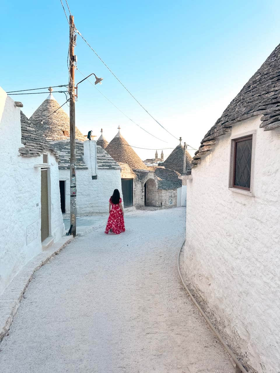 Woman in a pink, red, and white dress walking between traditional trulli houses in Alberobello