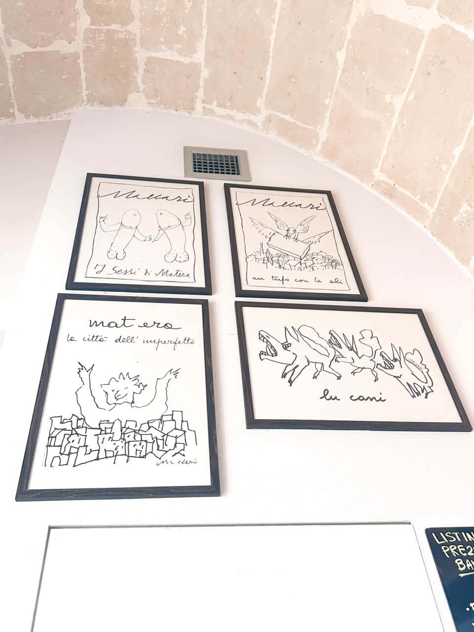 Framed illustrations inspired by Matera displayed on a white wall beneath a vaulted stone ceiling at Gahv&egrave; coffee & drink