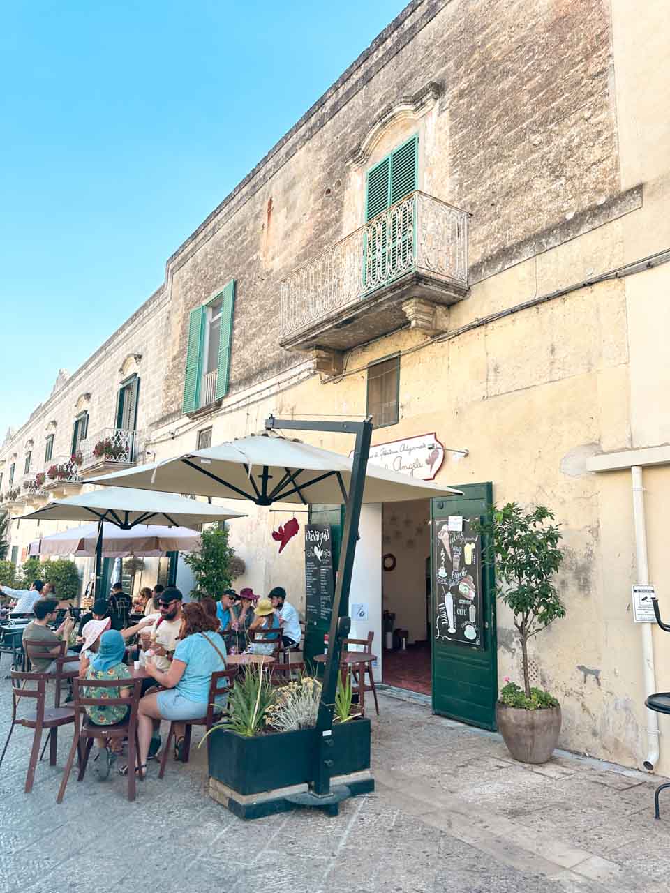 People sitting outside I Vizi degli Angeli on a sunlit square in Matera's historic centre