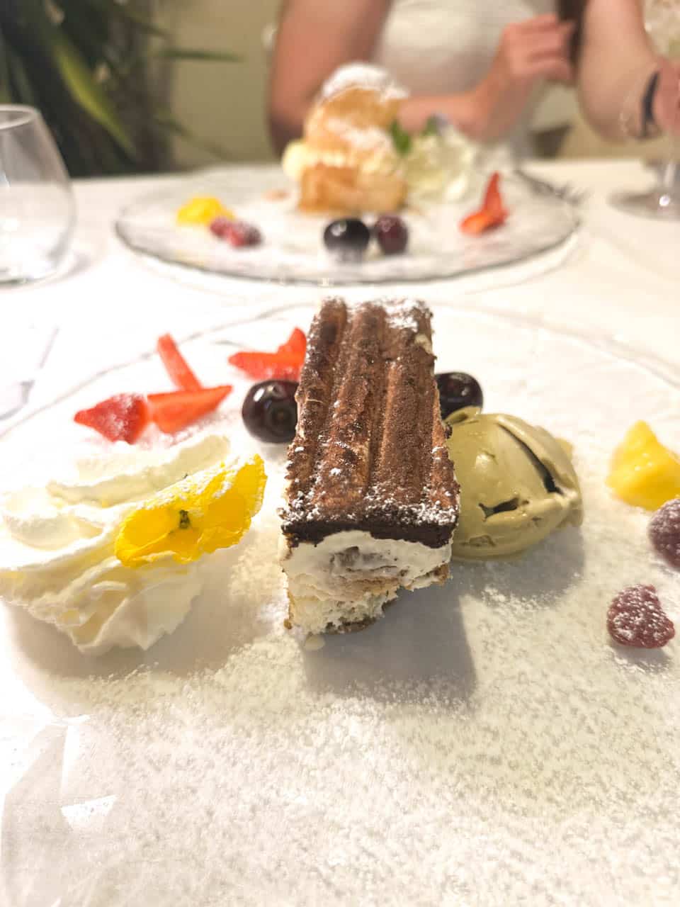 A plated tiramisu served with pistachio gelato, whipped cream, and fresh fruit at San Biagio Ristorante in Matera