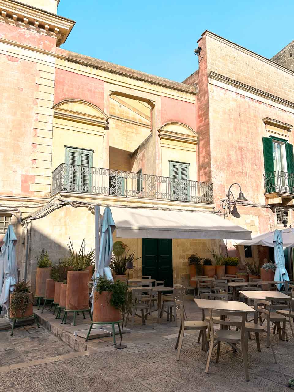 Outdoor tables beneath a historic pink stone building in Matera's old town