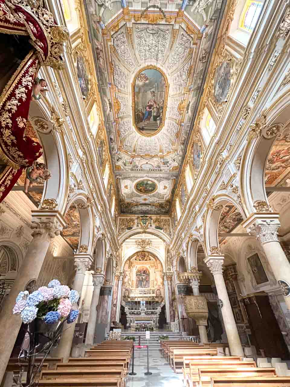 The ornate Baroque interior of Matera Cathedral with a frescoed ceiling and rows of wooden pews