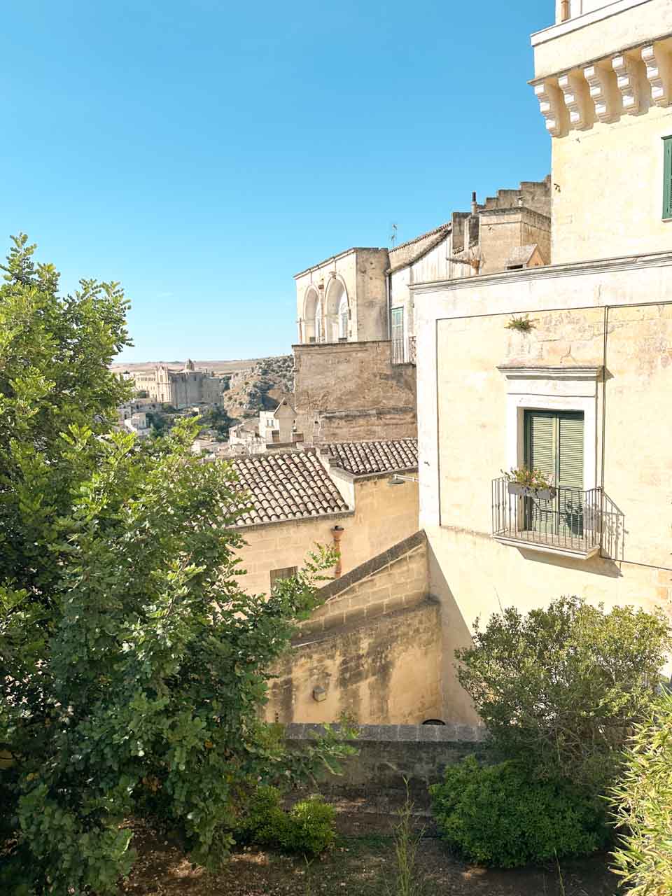 A view across Matera with stone buildings and greenery in the foreground