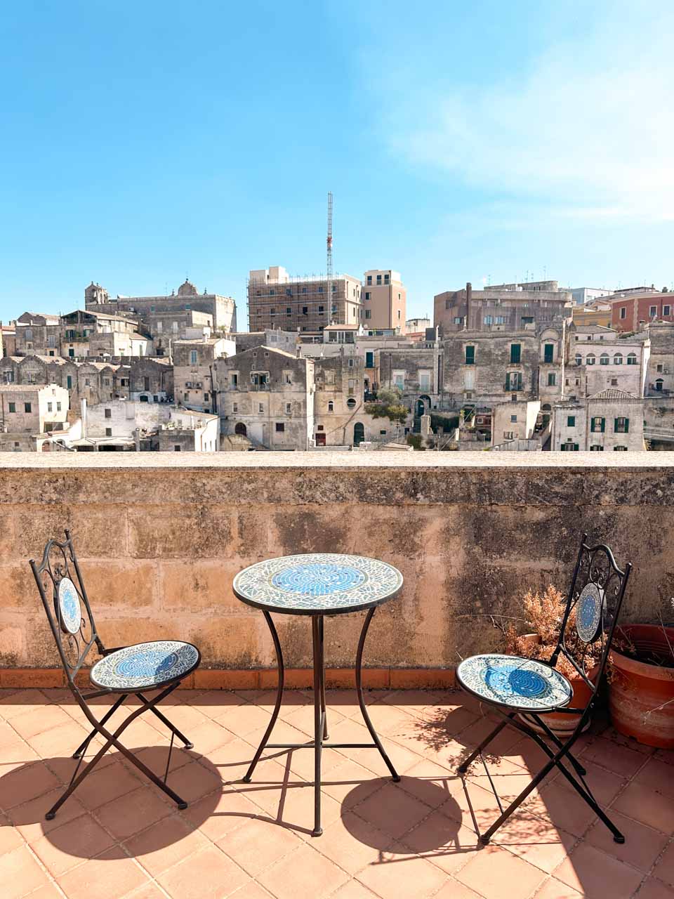 A small mosaic table and two chairs on a terrace overlooking the stone buildings of the Sassi in Matera
