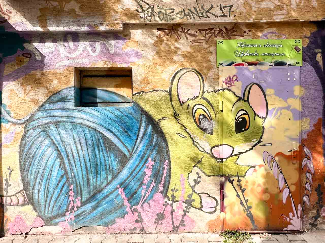 Colourful street art of a green mouse beside a giant blue ball of yarn in Sofia, Bulgaria
