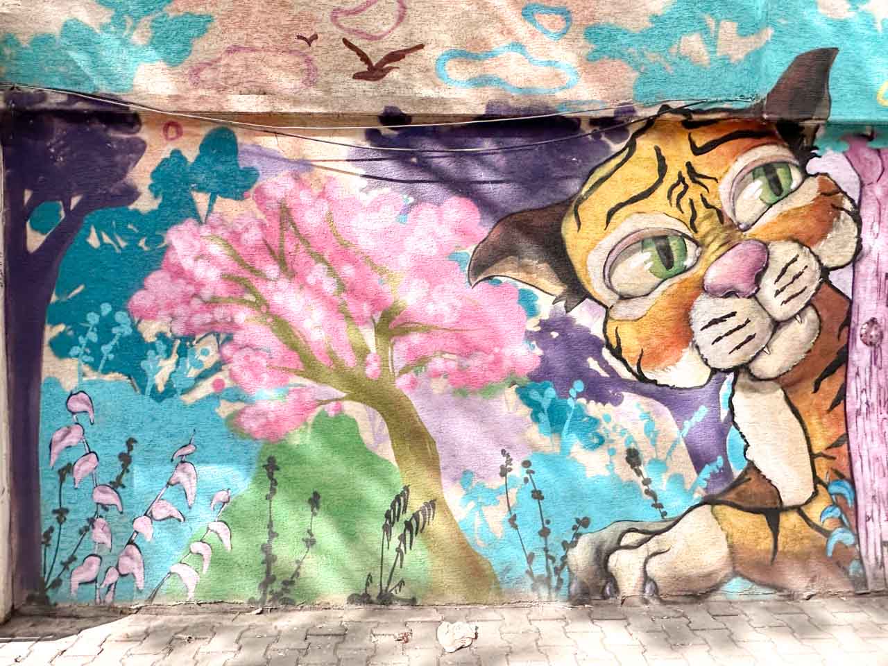 Colourful street art of a large orange cat beside a pink flowering tree in Sofia