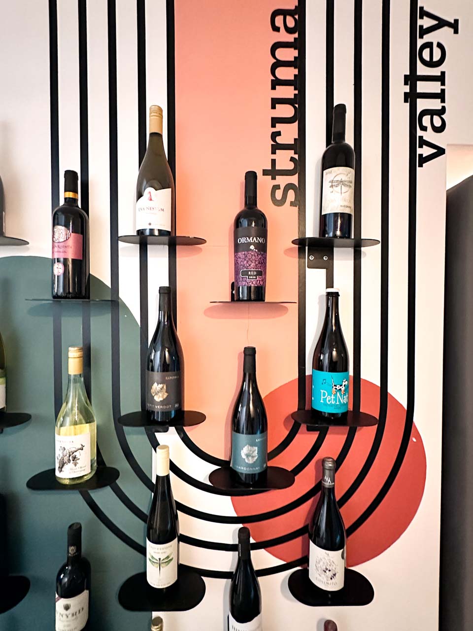 Bottles of Bulgarian wine displayed on individual wall shelves against a colourful geometric design inside the Wine Generator shop in Sofia