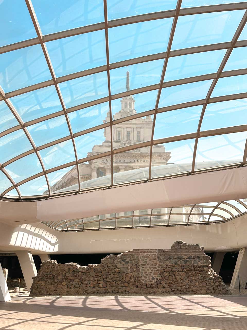 Ancient Roman ruins of Serdica beneath the glass dome of the Serdika metro station, with the former Communist Party House visible above