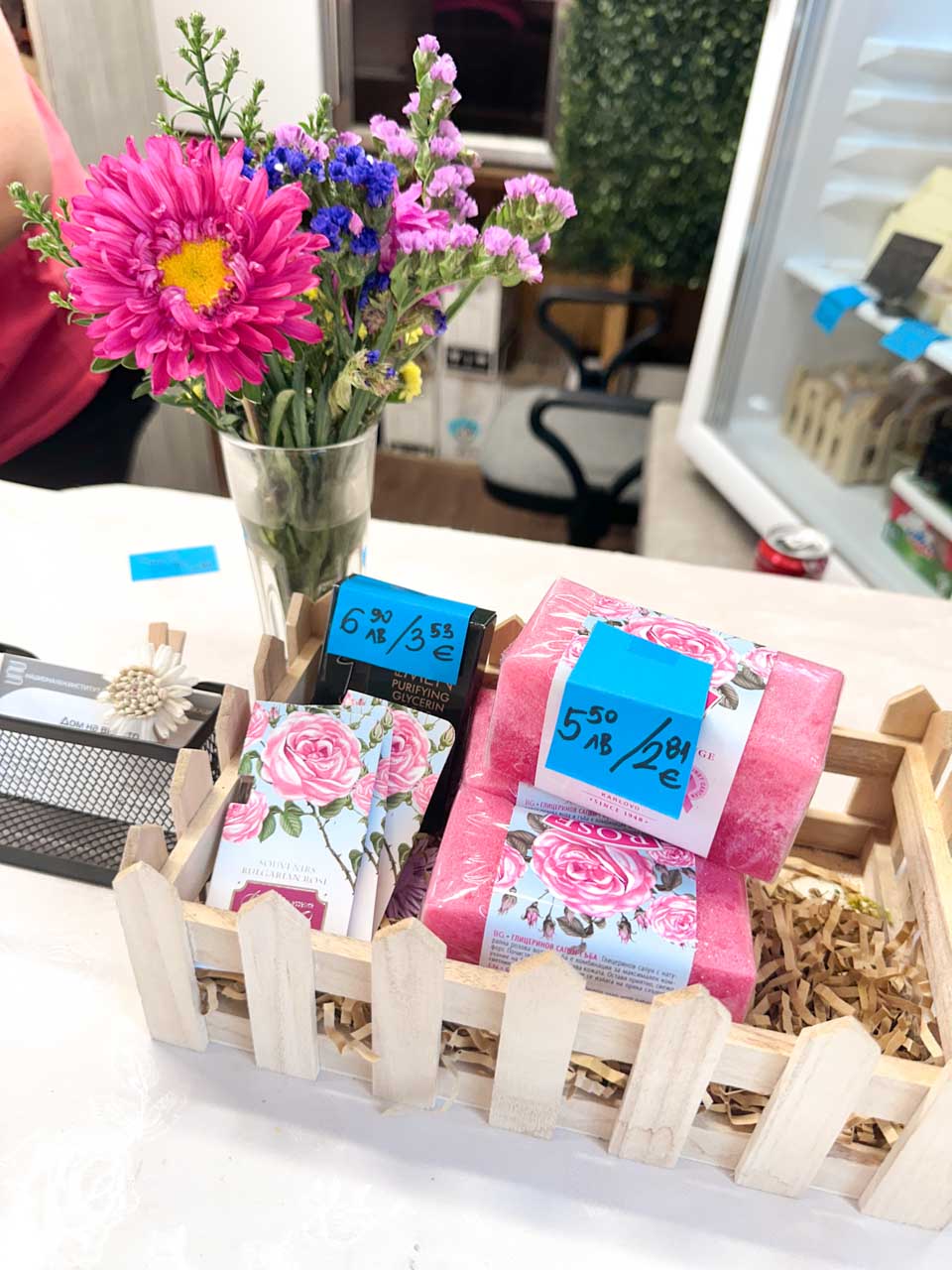 Colourful flowers and rose-themed products displayed for sale in a small wooden crate