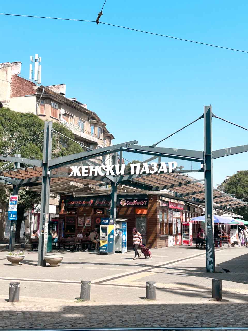 The entrance to Zhenski Pazar, or Women&rsquo;s Market, with stalls and shoppers on a sunny day in Sofia