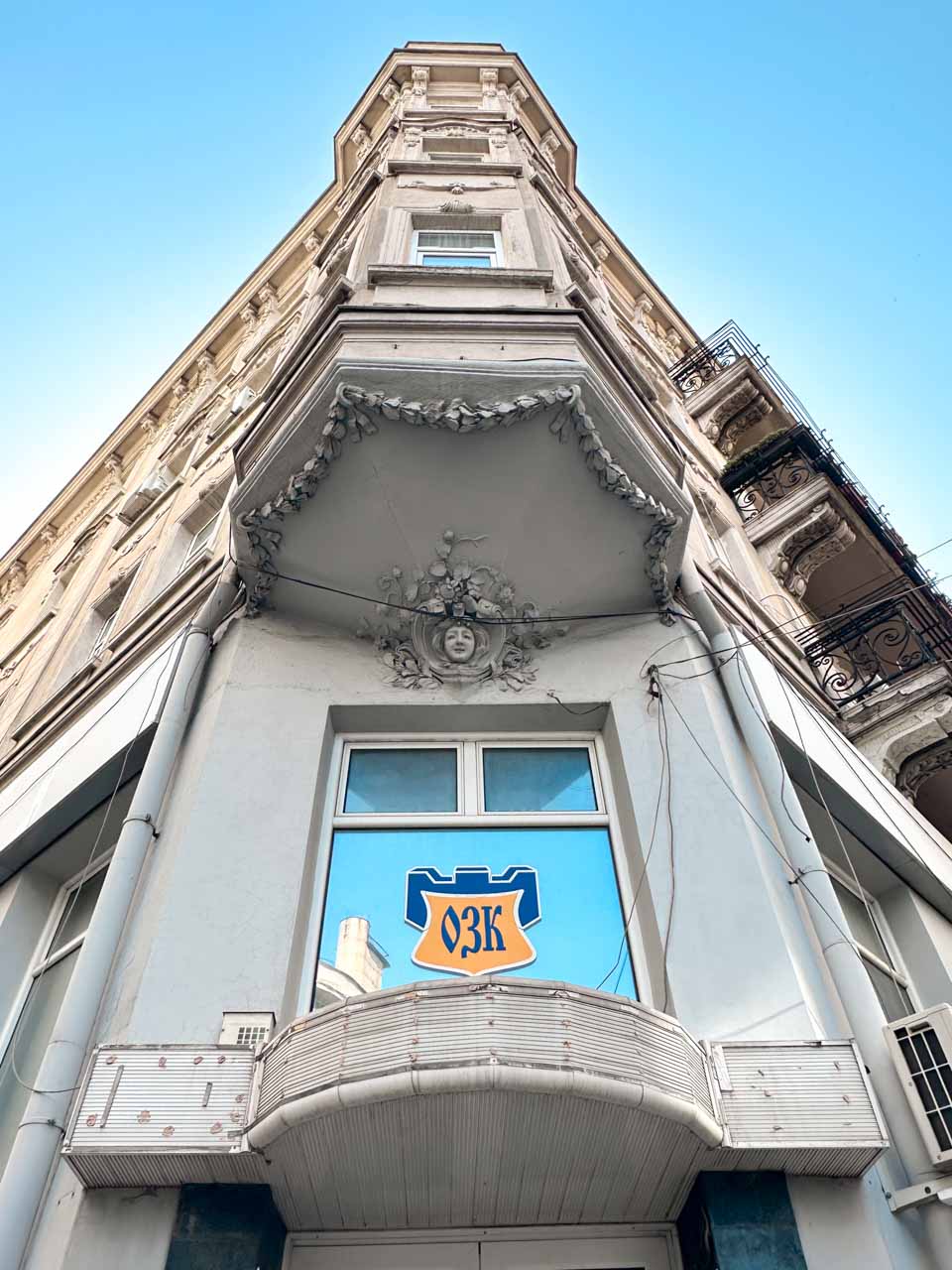 Looking up at the ornate corner fa&ccedil;ade of a historic building in Sofia, decorated with floral details and a sculpted face